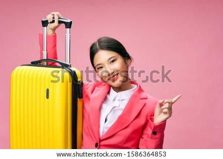 Yellow suitcase woman of Asian appearance glasses travel pink background