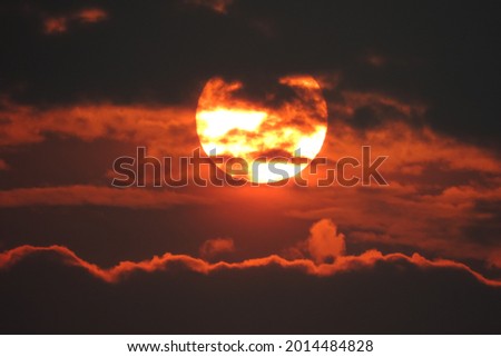 Yellow Sun among dark clouds on red black background
