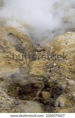Yellow surface of soil and rocks in a mountain gorge near geothermal springs. Steam over natural hot springs. Nature of the Russian Far East. Kamchatka Territory, Russia. Beautiful natural background.