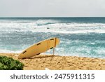 A yellow surfboard is propped against a pole by the beach