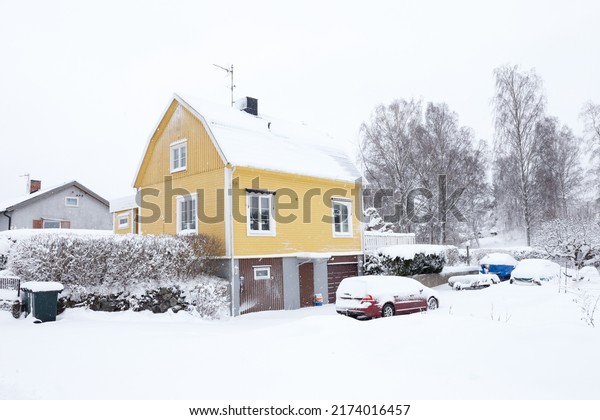 Yellow Swedish two-story single family house with\
a broken roof constructed in the late 1940s during snowfall in the\
winter season.