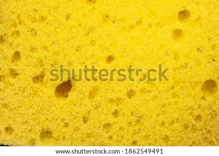 Yellow synthetic kitchen sponge with holes macro shot top view.