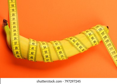 Yellow tape around banana isolated on orange background. Slim body and weight loss concept. Banana with yellow tape for measuring figure. Centimeter ruler spinned around fruit. Healthy food concept.