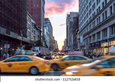 Yellow taxi cabs speeding down Broadway during rush hour in Manhattan, New York City with colorful sunset sky in the background