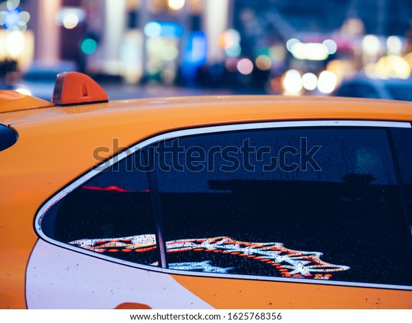 Yellow taxi car with reflections of LED\
advertising in tinted windows. Multi-colored festive lights in\
bokeh on background. New Year or Christmas decorations on street.\
Evening in city. Moscow,\
Russia