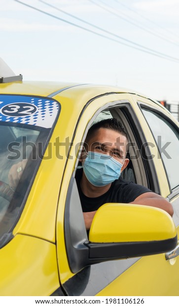 Yellow taxi. Latino taxi driver sitting\
with a mask for protection against the covid19\
flu.