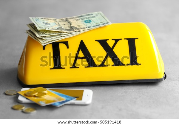 Yellow taxi roof sign with phone,\
credit cards and money on gray background,\
closeup