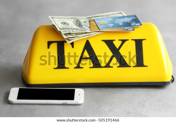 Yellow taxi roof sign with\
phone, credit cards and American dollars on gray background,\
closeup