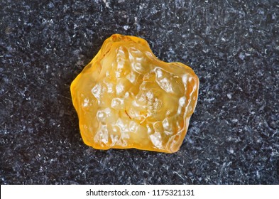 Yellow Tektite Specimen On Dark Granite Background Close-up. Libyan Desert Glass