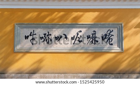 Yellow temple wall with mantra and sunny shadows, the six Chinese characters is the transliteration of Om mani padme hum.