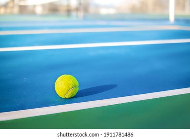 Yellow Tennis Ball Next To Sideline In Outdoor Tennis Court, Closeup. Defocused And Abstract Blue And Green Rubberized Ground Surface For Shock Absorption. Tennis Sport Texture. Selective Focus.