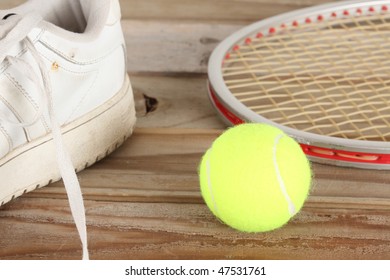 Yellow tennis ball and old white tennis shoe with aluminum racket on a weathered wooden plank deck - Powered by Shutterstock