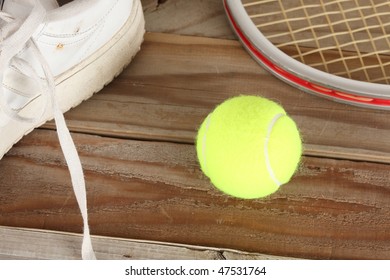 Yellow tennis ball and old white tennis shoe with aluminum racket on a weathered wooden plank deck - Powered by Shutterstock