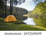 Yellow tent on the bank of a forest river. Spring trip to the national park.