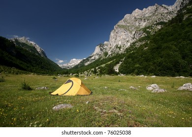 an yellow tent on a green meadow at the foot of a mountain. Ropojana Valley, Prokletije Mountains, or Albanian Alps, Montenegro