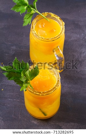 Yellow tomato cocktail with celery, spices, salt and ice, vertical