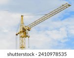 It is yellow tower crane  working in sunny day. There are the clouds in a blue sky. It is close up view.  It is midday time.