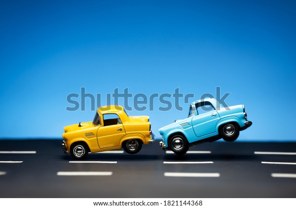 Yellow toy car and a blue\
car on a blue background and on a road. Blue car hits to yellow car\
from behind.