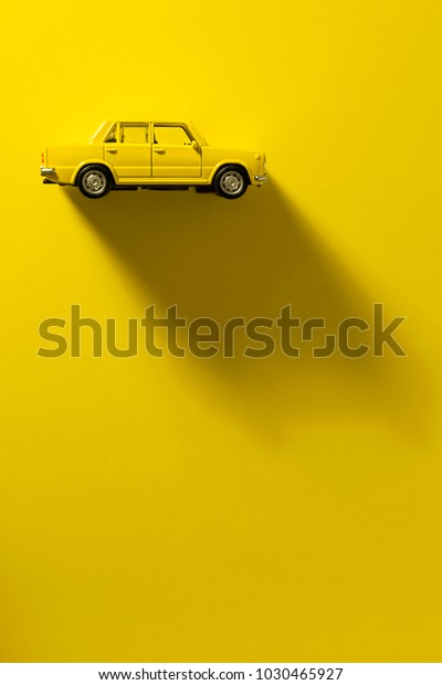 Yellow toy car on a yellow background with long\
and side shadow.