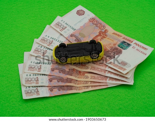 a yellow toy car is upside\
down on a stack of Russian money. Five thousand rubles, bills. The\
concept of a car accident, automobile repair, payment of road\
tax.