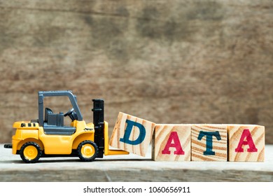 Yellow toy forklift hold letter block D to complete word data on wood background