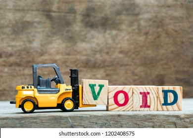 Yellow toy forklift hold letter block V to complete word void on wood background