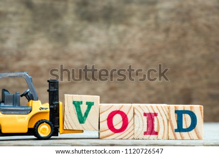 Yellow toy forklift hold letter block V to complete word void on wood background