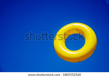 Yellow toy ring against the sky. Zero hanging in the air. Children's toy close-up.Yellow bagel on a bright blue background. Toy ring in the air. Bagel close up