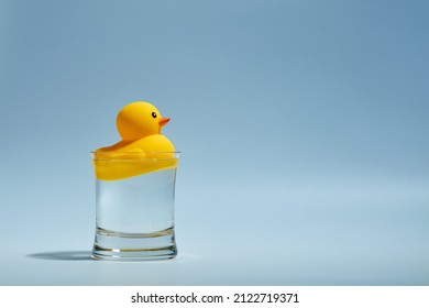 Yellow toy rubber duck floating in a glass of water.