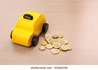 Yellow Toy Taxi Cab And Coins On Wooden Background