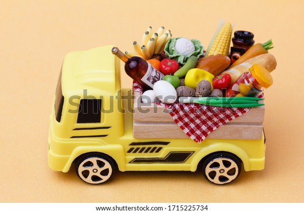 A yellow toy truck\
delivering food and drinks in a wooden box. Food supply  and food\
donation concept.