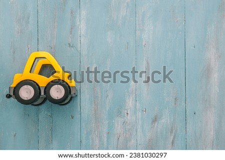 Yellow toy vehicle. Vintage style turquoise blue wooden background with copy space