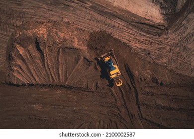 Yellow tracked bulldozer performs earthworks - aerial view shot. Yellow tracked tractor rakes the ground to build an asphalt road. Earthen bulldozer works during the construction of the route road.