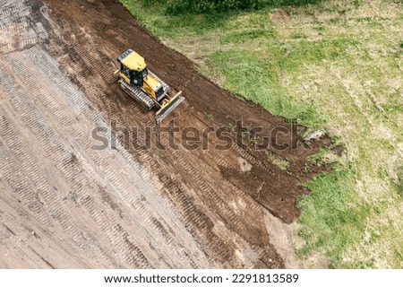 yellow tracked bulldozer performs earthworks on construction site. aerial view from flying drone.