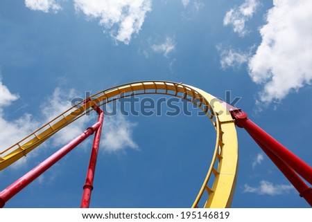 yellow tracks of steel roller coaster with red steel supporting tubular against blue sky with white cloud