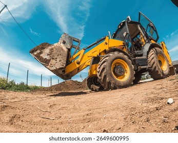 Yellow tractor loader is transporting soil from construction site. Side view. Clearing area for construction