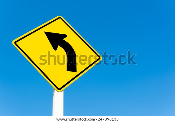 Yellow\
traffic left curve sign on blue sky\
background.