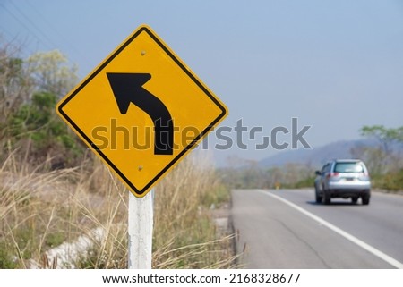  Yellow traffic sign with arrow left curve symbol beside the rural road to warn drivers to know the way ahead has a left curve. Concept : Warning traffic sign for transportation.                      
