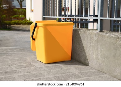 Yellow Trash Bin Near Fence Outdoors On Sunny Day