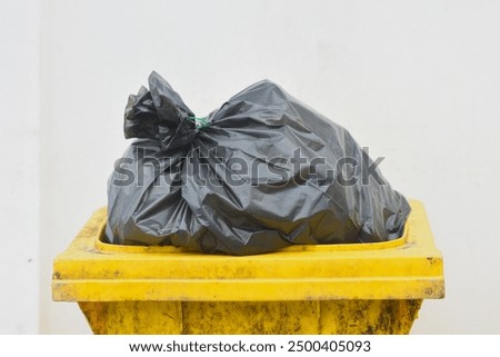 Yellow trash can with black plastic garbage bag