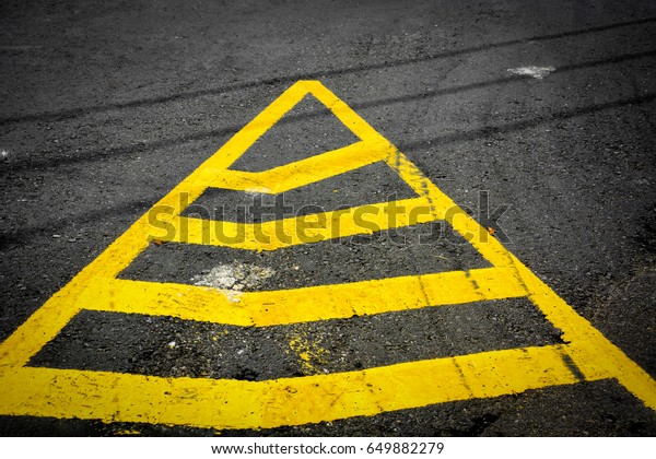 yellow triangle no parking lines painted on black\
asphalt road with tire\
tracks