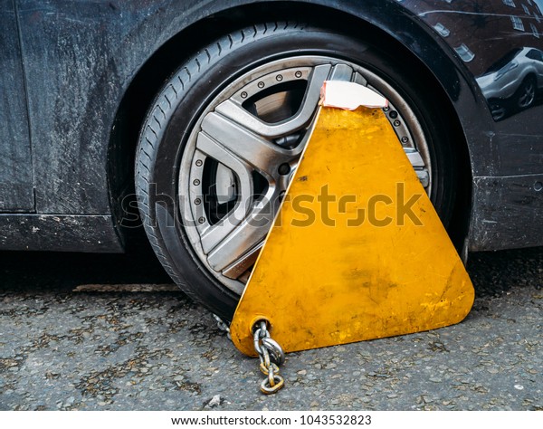 Yellow triangle wheel clamp locked\
with messing lock and chain on an illegally parked\
car.