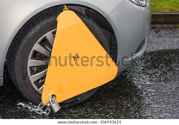 Yellow triangle wheel clamp locked\
with messing lock and chain on an illegally parked\
car