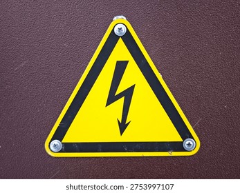 A yellow triangular caution sign shows a lightning bolt symbol to warn about electrical danger. It is attached with screws.