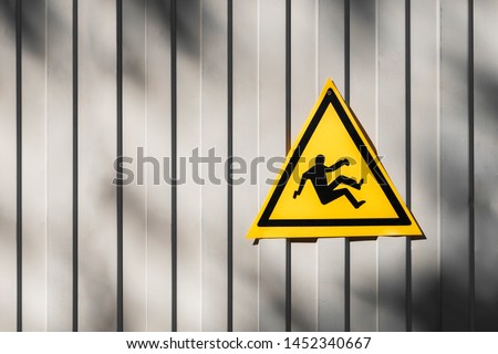Yellow triangular road sign warning for risk of falling hanging on the gray fence. triangular traffic sign warning for danger of falling or steep grade. Yellow falling man -Warning hazard sign
