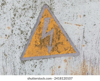 A yellow triangular sign with a lightning bolt is painted on an old gray metal surface, which warns of high voltage.