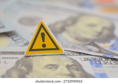 a yellow triangular warning sign with US one hundred-dollar banknotes, highlighting economic alerts or financial fraud
