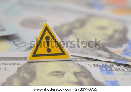 a yellow triangular warning sign with US one hundred-dollar banknotes, highlighting economic alerts or financial fraud