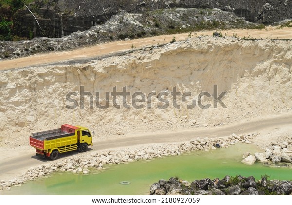 Yellow truck busy transporting white sand on\
limestone cliffs