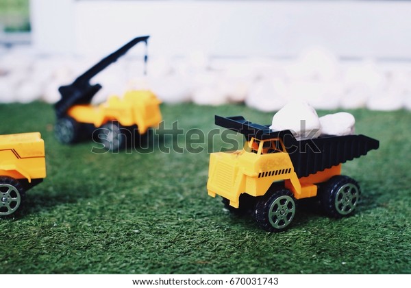 Yellow truck in construction is\
loading white stone. Truck is driving on green grass in\
construction site. Civil engineering are working in construction\
area.